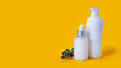 Sarı zemin üzerinde, üzerinde küçük bir okaliptüs dalı bulunan beyaz plastik kozmetik pompalı ve damlalıklı şişeler