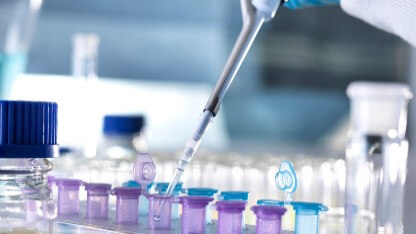 Bir analitik bilimcinin elinde, kozmetik ürün numunesini ağır metal testine hazırlamak üzere mor ve mavi numune şişelerine sıvı pipetlemek için bir pipet tutuyor.